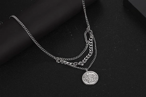 Close-up of layered silver titanium steel necklace with punk coin pendant on black stand