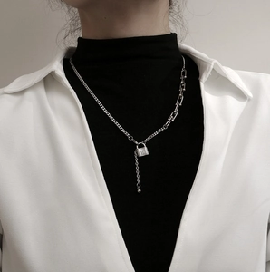 Detalle de collar de cadena plateada con diseño asimétrico y colgante de candado