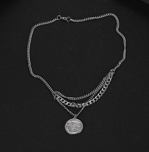 Close-up of silver layered necklace featuring flat curb chains and a vintage coin pendant