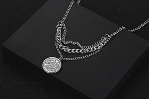 Close-up of layered silver titanium steel chains with a vintage coin pendant detail
