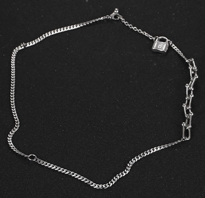 Detalle del collar plateado asimétrico con eslabones en U y pequeño colgante de candado