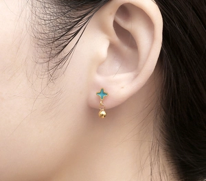 Detail of a blue star earring with gold bead drop worn on a female earlobe