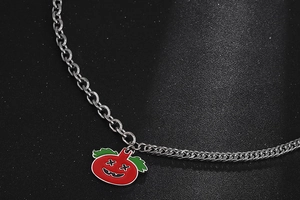 Macro shot of punk tomato pendant with green leaves on bright metallic chain link