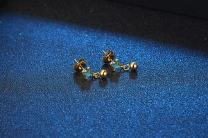 Detail of gold stud earrings featuring a blue star enamel pattern and small round gold bead