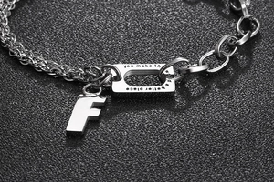 Detail of silver titanium steel bracelet with letter F charm and engraved quote tag