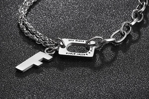 Close-up of silver steel bracelet with F letter charm and inspirational quote tag