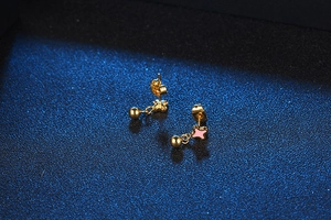 Macro shot of gold-tone mini stud earrings with pink floral enamel and round metal pendant
