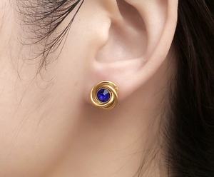 Close-up of golden spiral earrings with deep blue center stone worn on ear for detail