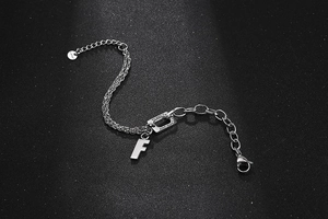 Macro detail of stainless steel bracelet featuring letter F charm and engraved quote tag