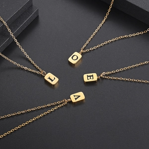 Goldenes Set aus rechteckigen Buchstabenanhängern mit feiner Kette auf schwarzem Grund