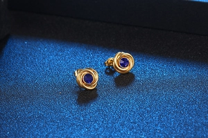 Detail of gold rose stud earrings with deep blue round gemstones on a textured surface