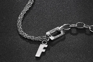 Macro detail of mixed chain necklace with letter F pendant and engraved quote plaque