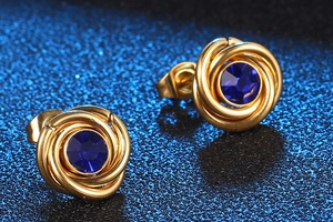 Macro detail of gold-plated spiral stud earrings with deep blue crystal and butterfly back