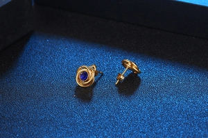 Macro detail of gold spiral stud earrings with deep blue round gemstone settings