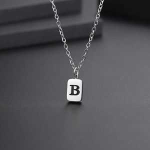 Macro view of minimalist silver titanium necklace with square pendant engraved with letter B