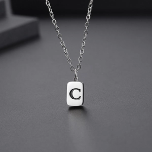 Detailed close-up of a silver rectangular pendant featuring an engraved letter C on a chain