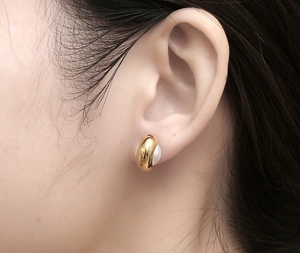 Gros plan de boucles d'oreilles dorées polies avec perle blanche sur le modèle