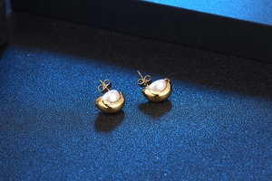 Détail de puce d'oreille dorée avec perle blanche sur surface bleue élégante