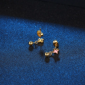 Minimalist gold stud earrings with pink star charms and small ball drop on blue background
