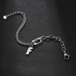 S.steel lettering chain bracelet with an F-pendant on a textured black surface
