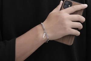 Detail eines silbernen Titanstahlkettenarmbands mit rundem Buchstaben F Anhänger