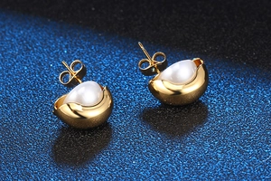 Détail de boucles d'oreilles dorées avec perles blanches et fini métal poli