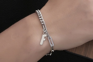 Nahaufnahme eines silberfarbenen Gliederkettenarmbands mit einem großen F-Buchstabenanhänger