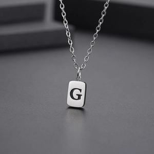 Macro shot of silver titanium steel necklace featuring a rectangle pendant with letter G