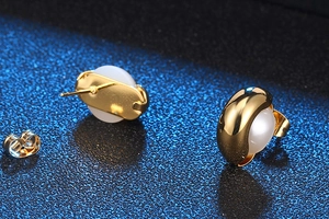 Vue macro de boucles d'oreilles dorées avec pierre blanche et fermoirs papillon