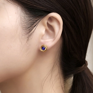 Golden swirl stud earrings with round blue stone on a female model with natural soft lighting
