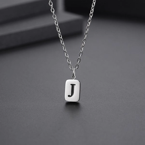 Macro detail of silver rectangular pendant with engraved black letter J on steel chain