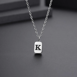Macro shot of silver titanium steel rectangular pendant with engraved letter K on a cross chain