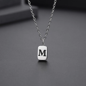 Detailed close-up of a silver stainless steel rectangular pendant with letter M engraving