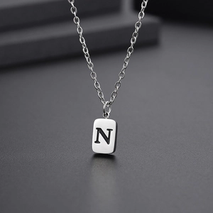 Macro shot of rectangular pendant with engraved black letter N on silver stainless steel chain