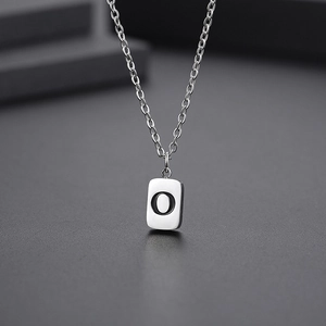 Macro detail of a silver stainless steel necklace featuring a matte rectangular letter O pendant