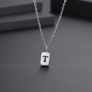 Macro detail of silver titanium steel necklace featuring a rectangular letter T pendant