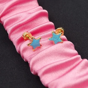 Detail of blue and glittery star stud earrings with gold screw-back on pink ribbon
