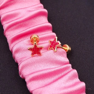 Miniature gold star stud earrings with red glitter inlay on a pink silk ribbon