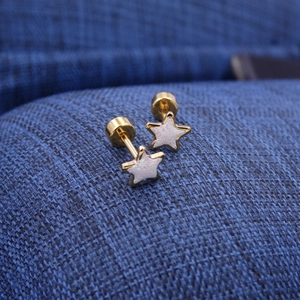 Macro detail of star-shaped titanium steel studs with sparkling pink enamel and gold finish