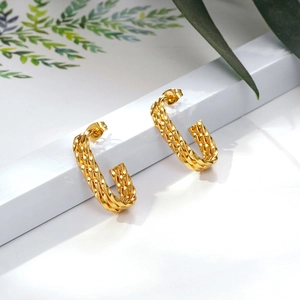 Golden twisted hoop earrings with elegant woven texture on minimalist white stand