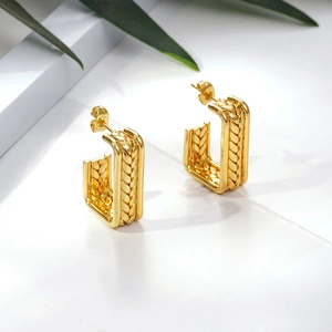 Golden geometric earrings with woven wheat texture on elegant marble stone background
