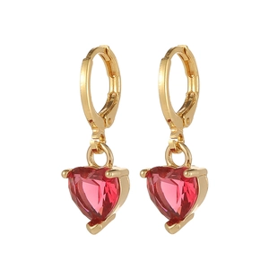 Détail de boucles d'oreilles huggie dorées avec zircons rouges en forme de cœur sertis à trois griffes