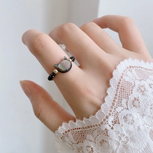 Detail of beaded cat ring with black mother of pearl on finger and white lace sleeve