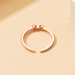 Dettaglio anello a fiocco in oro rosa con fascia regolabile su sfondo beige caldo