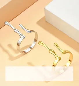 Close-up of adjustable fluid-style open rings in gold and silver finishes on white props
