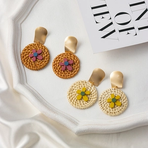 Bohemian rattan flower earrings set with matte gold metal studs on a white tray