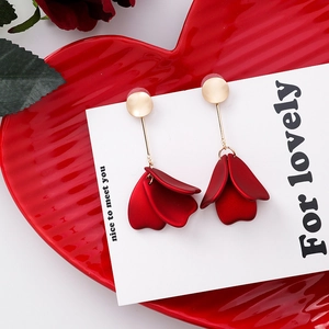 Close-up of red petal earrings with gold metallic accents on a red ceramic dish
