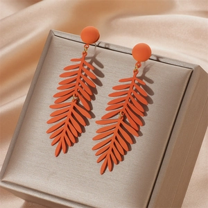 Detailed macro view of matte orange leaf drop earrings on champagne silk fabric background
