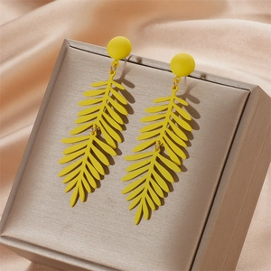 Detail view of yellow matte leaf drop earrings on a champagne silk background