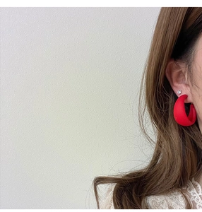 Close-up of a matte red C-shaped earring on model featuring a smooth frosted texture